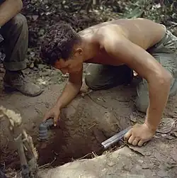 An American soldier prepares to check a tunnel, with a flashlight and a pistol.